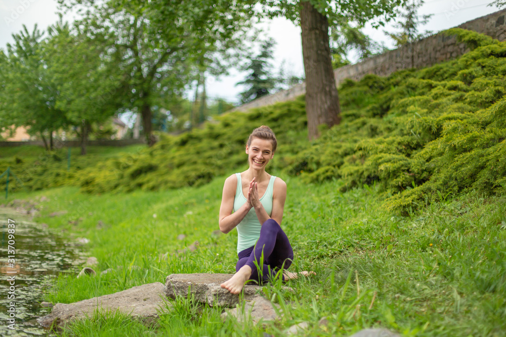 A young sports girl practices yoga on a green lawn by the river, yoga assans posture. Meditation and unity with nature A young sports girl practices yoga on a green lawn by the river, yoga assans posture. Meditation and unity with nature