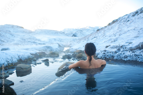 The girl bathes in a hot spring in the open air with a gorgeous view of the snowy mountains. Incredible iceland in winter
