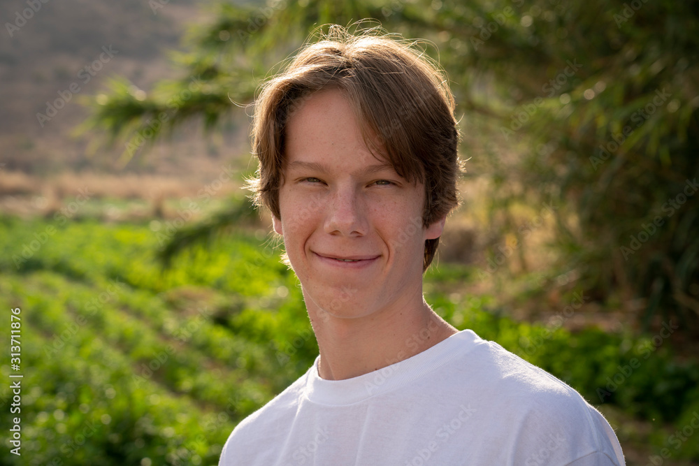A teenage boy smirks at the camera while backlight in the afternoon sun.