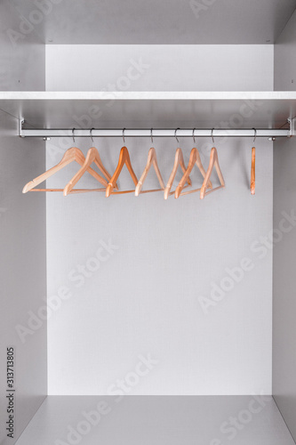 row of lacquered wooden light hangers for clothes hangs in wardrobe on metal rod. There's empty shelf on top. Accessories made of environmental material