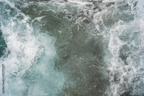 Raging blue water in a backwater with stones and white foam. © Artem