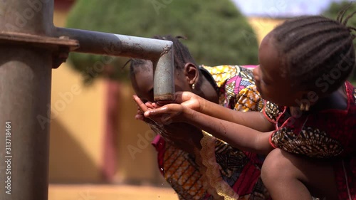 Two beautifully Dressed Little African Girls Sipping Water From a Tap