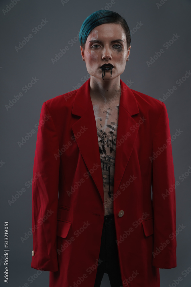 Obraz premium Studio photoshoot of a beautiful girl with blue hair and fashion makeup in a red jacket on a grey background. Fashion style