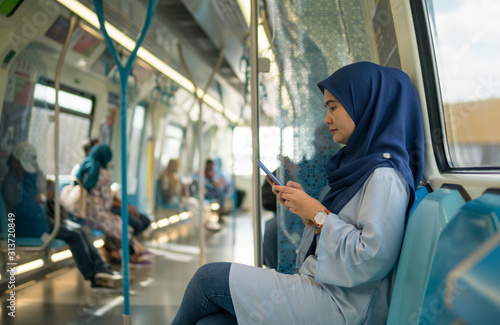 Young Muslim woman traveling inside subway train sitting while using phone. Transportation and technology concept. 