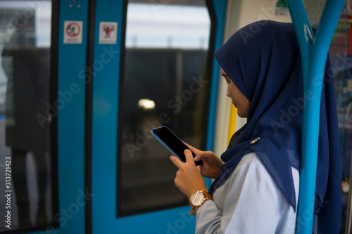 Young Muslim woman traveling inside subway train standing while using phone. Transportation and technology concept. 