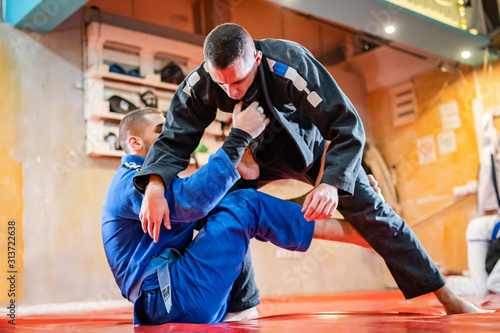 Two brazilian jiu jitsu BJJ athletes training practicing position drilling the technique from the guard sparring wearing blue and black kimono holding collar grip