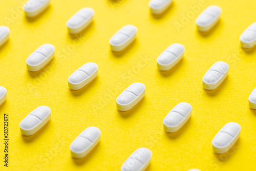 White pills or capsules lies in rows diagonal on yellow background