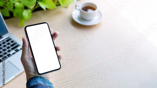 Mockup image blank white screen cell phone.man hand holding texting using mobile on desk at office.background empty space for advertise text.people contact marketing business,technology 