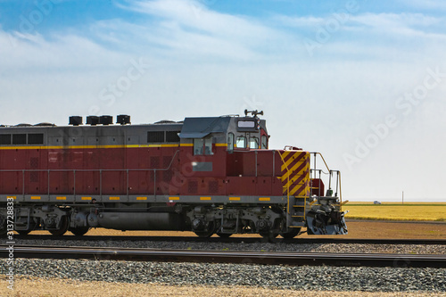 Vintage locomotive of a Canadian National Railways vintage freight train, red with yellow stripes. Moving towards right in the countryside.