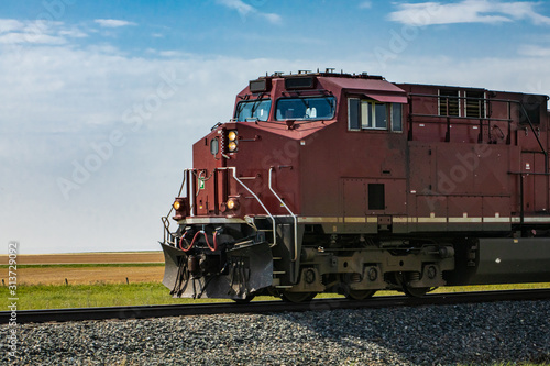 Vintage locomotive of a red Canadian National Railways vintage freight train, with headlights on, moving towards left. Copy space on the left.