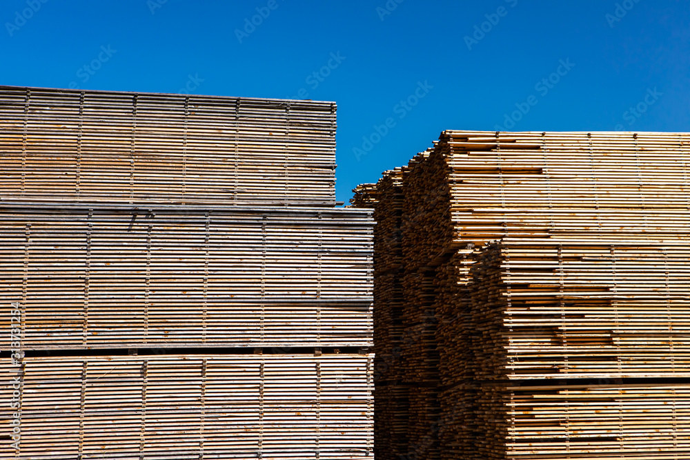 Long planks of pinewood are seen stored outdoors. Many sawn and treated boards in the yard of a sawmill. Stockpiled ready for distribution. Long planks of pinewood are seen stored outdoors. Many sawn and treated boards in the yard of a sawmill. Stockpiled ready for distribution.