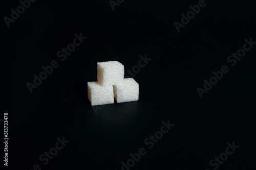 Three sugar cubes on a black background, a sweet additive to taste or a harmful and dangerous ingredient, diabetes, place for text