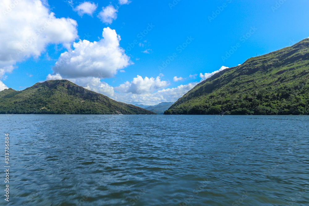 Beautiful landscape of blue water lake between two green mountains with a partly cloudy blue sky.
