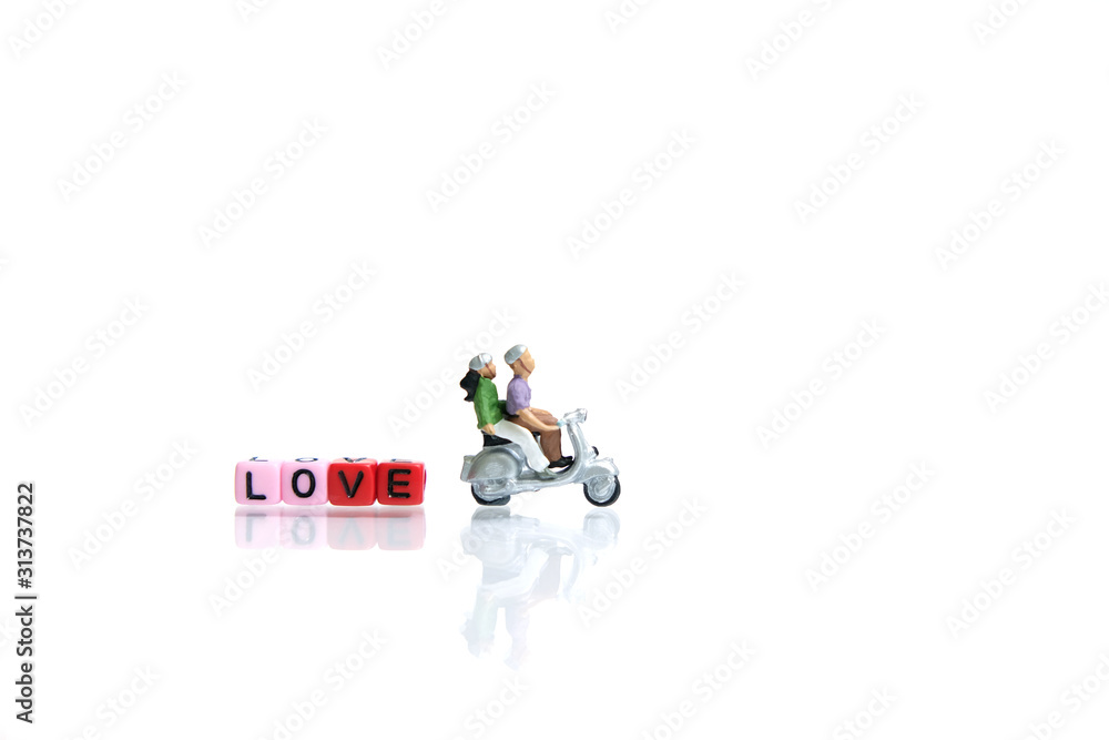 Fototapeta premium Miniature / toys photography for valentines day - young couple riding scooter with love beads word block on shiny white background