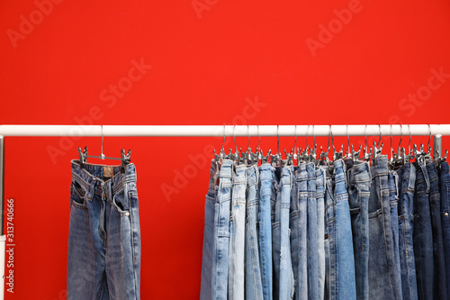 Rack with stylish jeans on red background