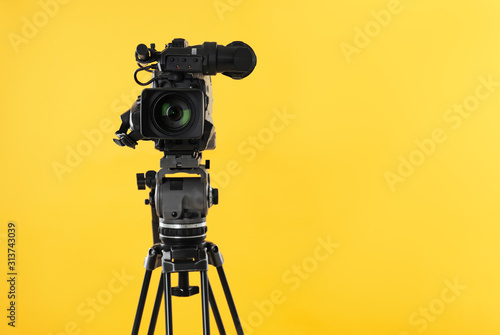Modern professional video camera on yellow background. Space for text photo