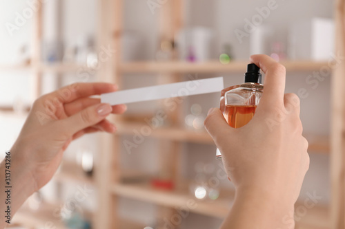 Woman with bottle of perfume and blotter indoors, closeup photo