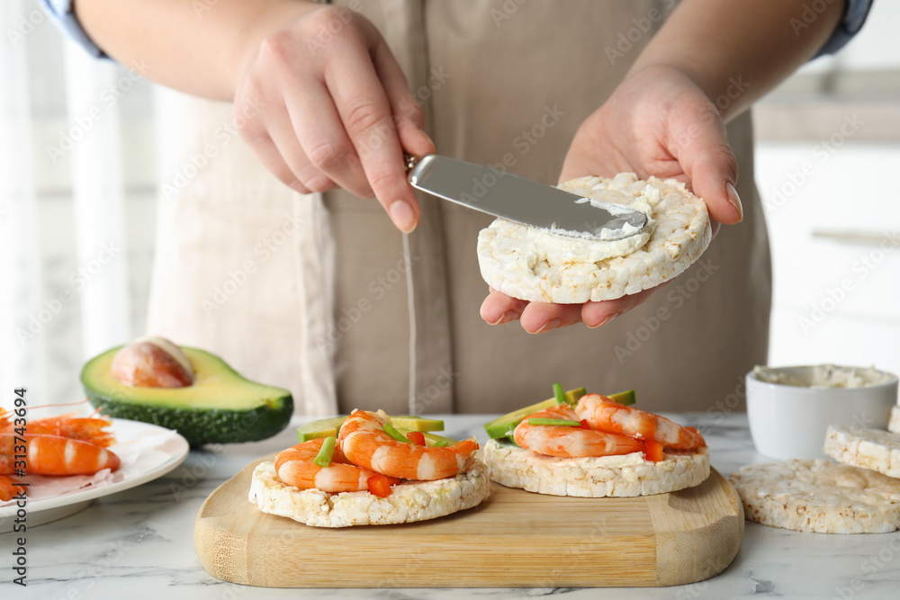 Woman spreading butter on puffed rice cake over white table indoors, closeup Woman spreading butter on puffed rice cake over white table indoors, closeup