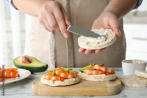 Woman spreading butter on puffed rice cake over white table indoors, closeup