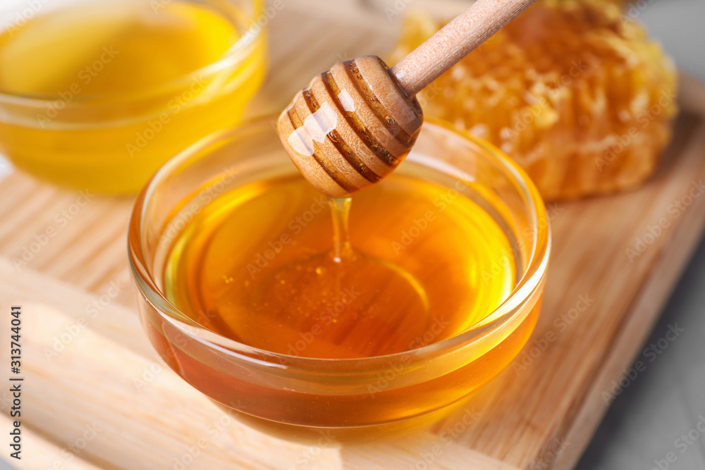 Dripping tasty honey from dipper into bowl on table, closeup Dripping tasty honey from dipper into bowl on table, closeup