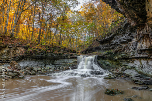 A beautiful waterfall in a rocky gorge surrounded by colorful fall leaves flows in the autumn woods of McCormicks Creek State Park in Owen County Indiana