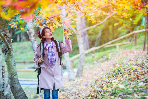 An Asian female tourist is happy to see the maple trees changing color in the garden. The morning sun in autumn