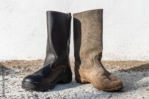 A pair of different boots outdoor. Contrast old and new, clean and dirty shoes.