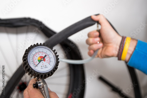 A person is inflating a bicycle inner tube wuth the help of compressed air and a pressure gauge. Wheel and hand seen in the background in soft focus.