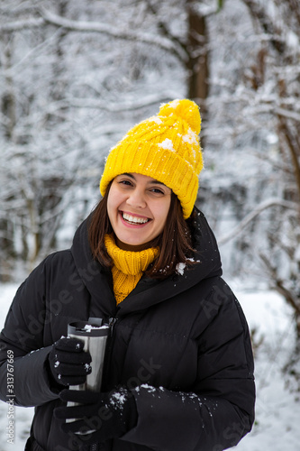 smiling woman in winter outfit drinking warm up drink from refillable mug