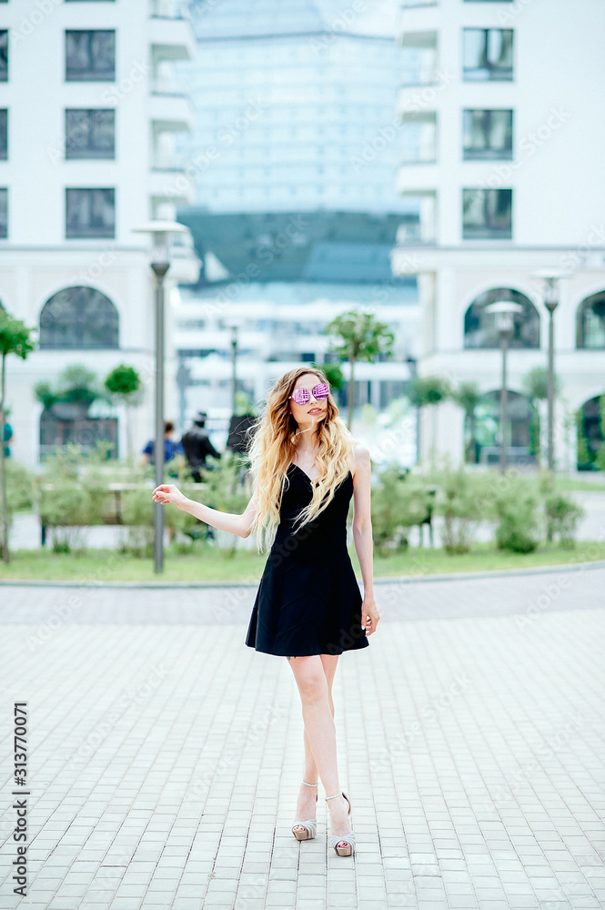 A beautiful girl of doll appearance in a black dress on a city street. Natural sunlight A beautiful girl of doll appearance in a black dress on a city street. Natural sunlight