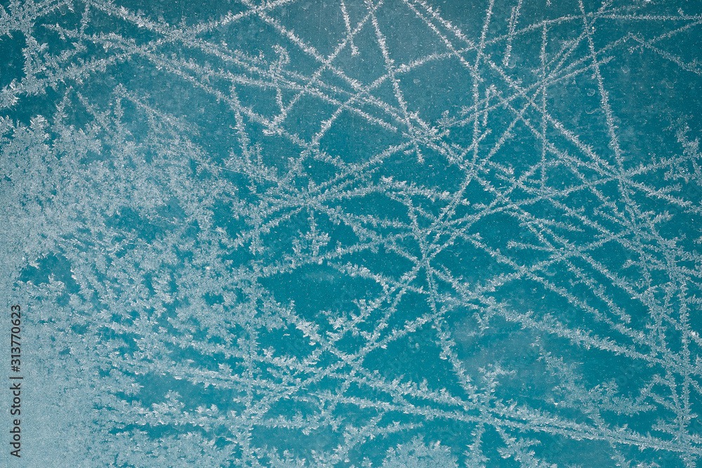 Frost pattern on glass of a window. Frozen ice forming during the cold weather on glass window. Blue background.