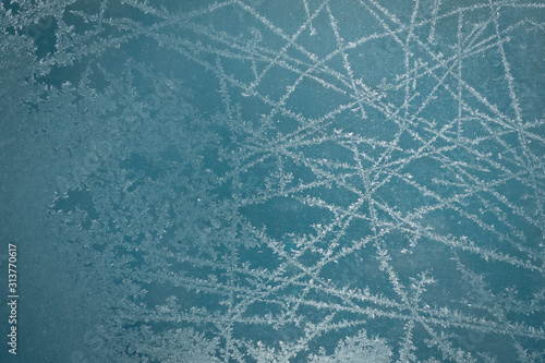 Frost pattern on glass of a window. Frozen ice forming during the cold weather on glass window. Blue background.
