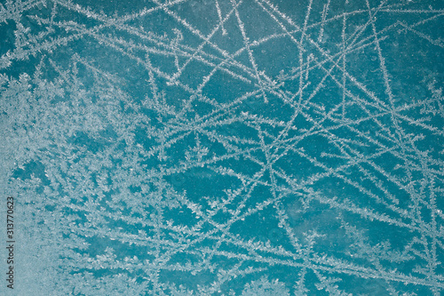 Frost pattern on glass of a window. Frozen ice forming during the cold weather on glass window. Blue background.