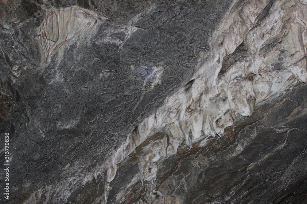 Fototapeta premium Gray karst cave. Rock formations in the cave, stalactites and stalagmites. Abstract gray grunge background. Stone texture background. Spotted abstract stone. Russia, Bashkortostan, a fairy cave