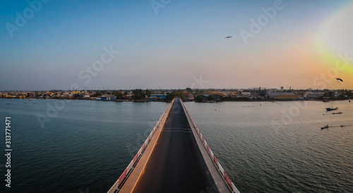 Aerial view of the road bridge over casamance river in Ziguinchor, Senegal, Africa during a sunset. Looking towards the city above the driving platform with yellow taxi crossing the bridge. © Anze