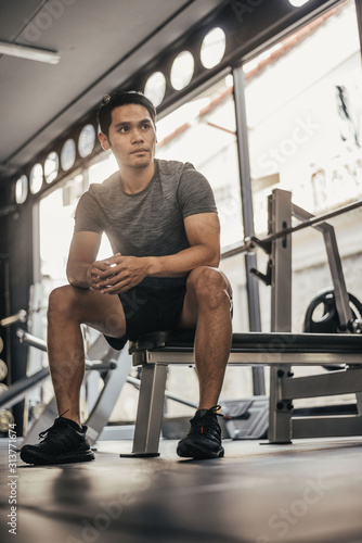 Young fitness man sitting in gym. asian sport man sitting and looking to outside in sportclub. 