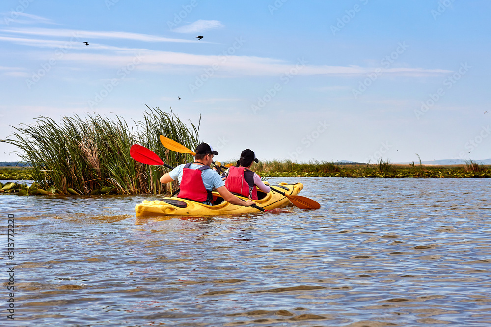 Man and a woman paddle yellow kayak on a river. Back view on couple kayaking on a river at summer