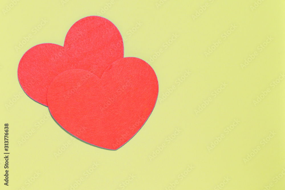Two red felt hearts on a pale yellow background close-up. Flat lay, copy space. Valentine's Day greeting card