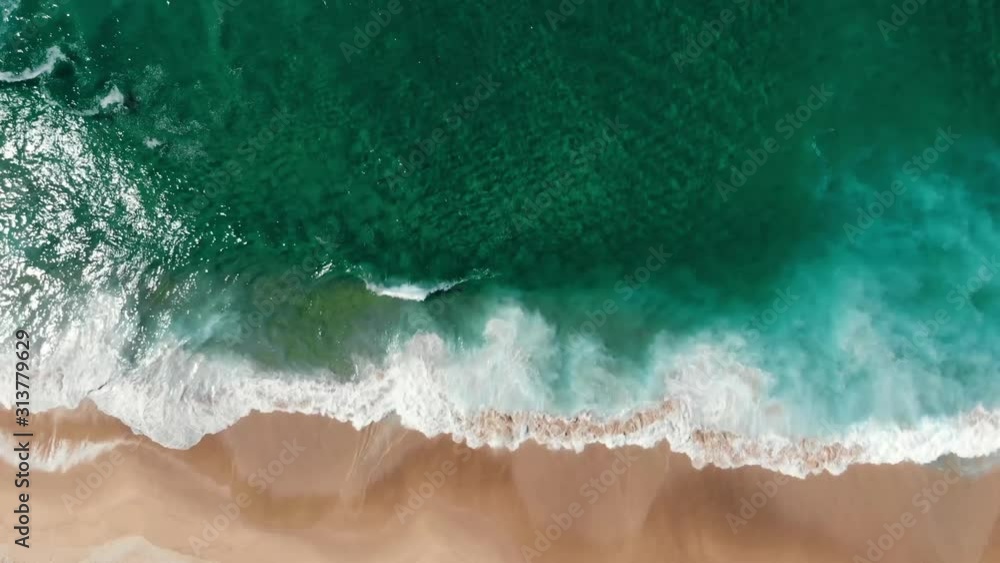 Aerial view of drone flying above beautiful beach with views of ocean waves and water crashing on to sandy beach from top angle
