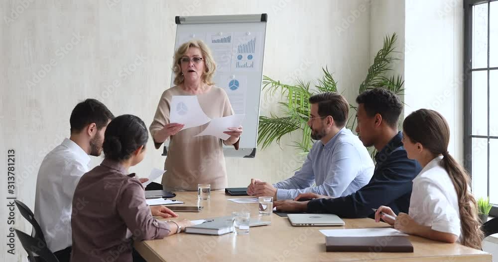 Middle aged businesswoman executive manager give papers at team meeting Middle aged businesswoman executive manager give papers at team meeting