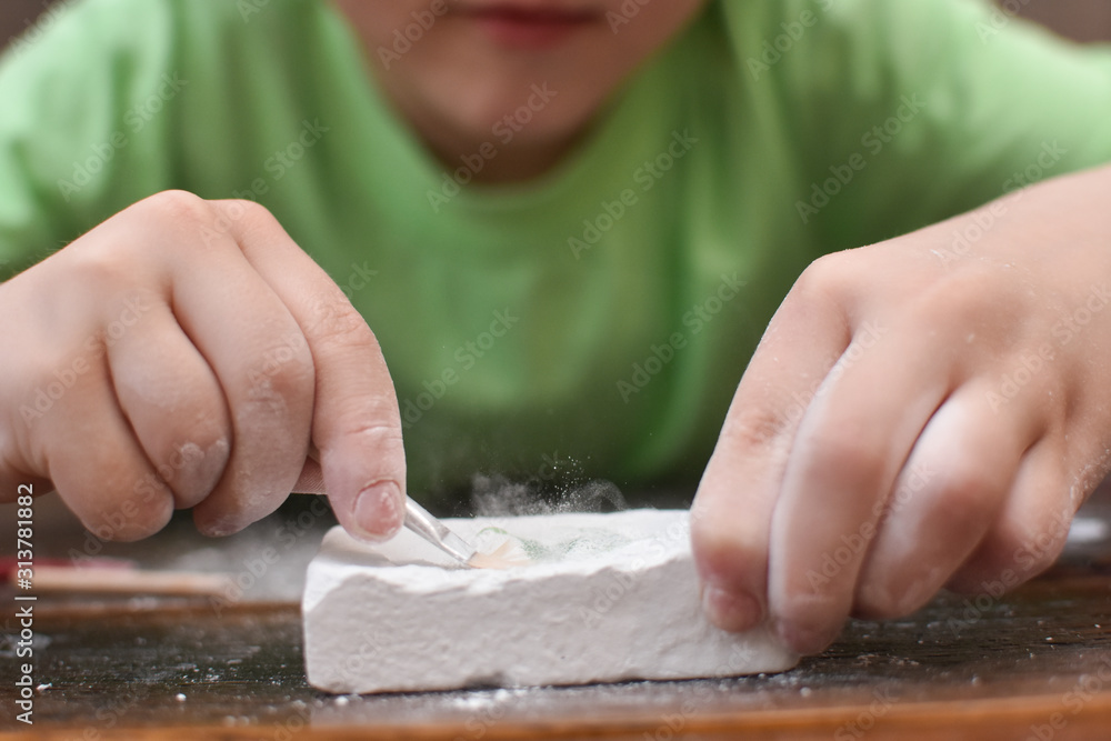 Child's hand is playing with the archaeological set. Child digging a dinosaur. Boy have fun with archaeology excavation kit Child's hand is playing with the archaeological set. Child digging a dinosaur. Boy have fun with archaeology excavation kit