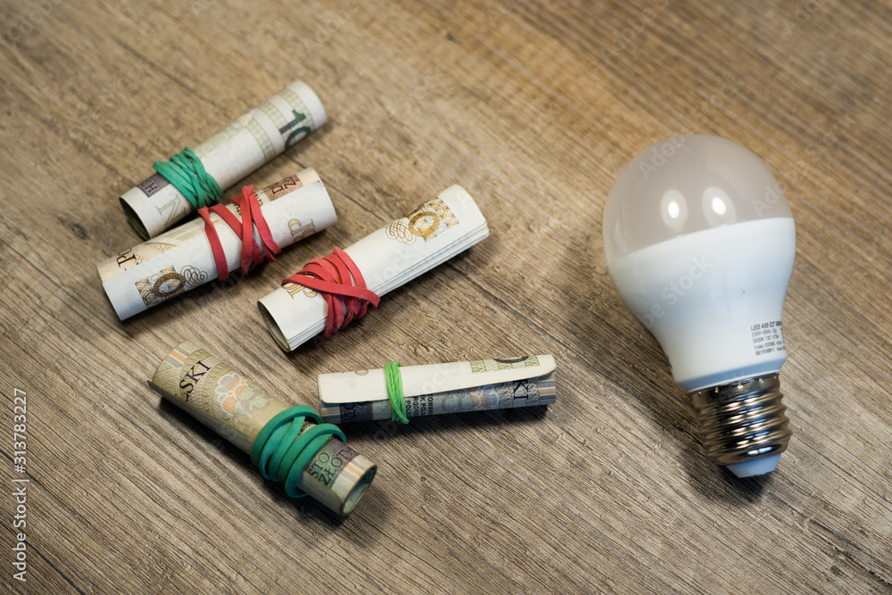 Naklejka premium Money rolled up with an elastic band with bulb on wooden table. Polish currency. Polish zloty banknotes. Polish money. PLN