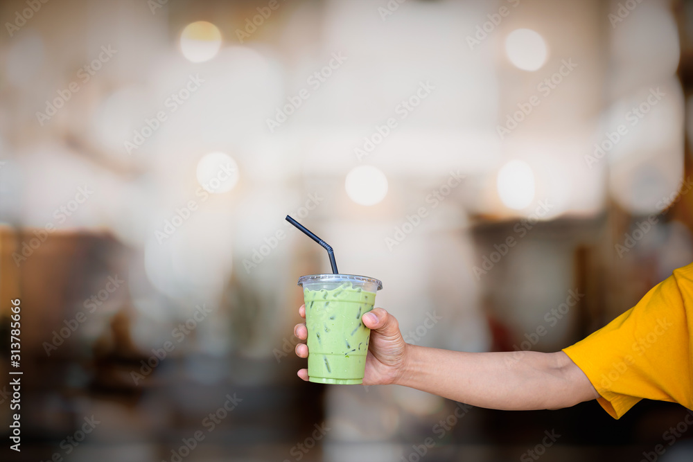 Green tea with mill plastic glass in hand with blurred cafe background. Green tea with mill plastic glass in hand with blurred cafe background.