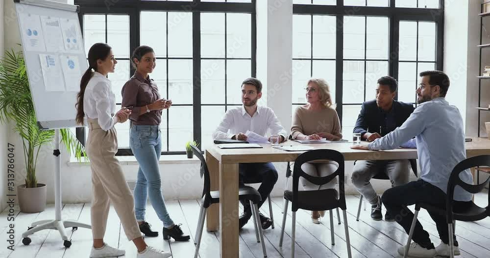 Two diverse ethnicity female colleagues give business presentation on flipchart