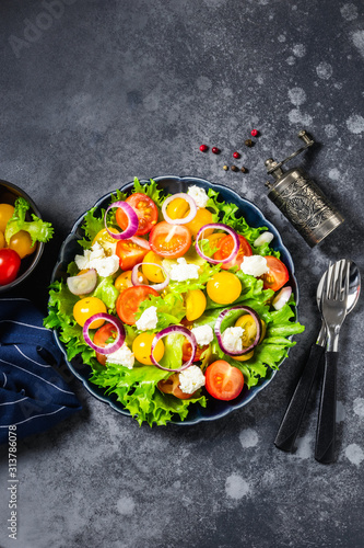 Fresh rainbow salad with feta cheese and lemon dressing on dark background. Top view, space for text.