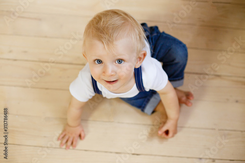 Little boy in wooden scandinavian interior on a wooden floor. Infant boy weared in casual denim. Small baby feet. Kid of one year old crawls on the floor. Small legs. First birthday