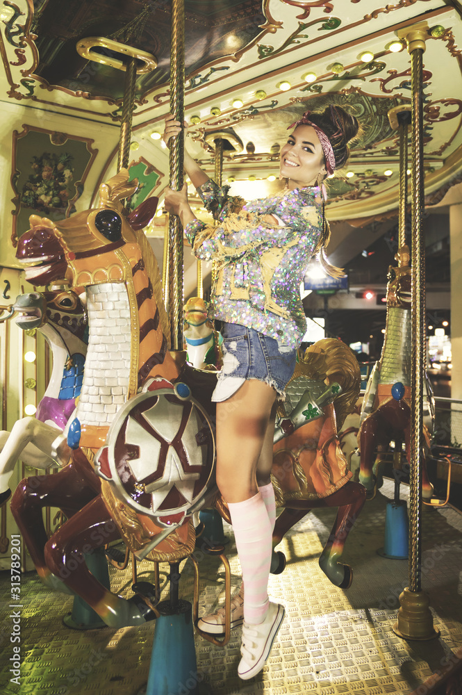 Stylish woman wearing sparkling jacket on the carousel - obrazy, fototapety, plakaty 