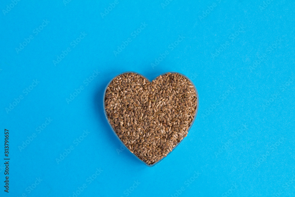 Flax seeds in the heart shape in the center of the blue background. Top view. Copy space. Flax seeds in the heart shape in the center of the blue background. Top view. Copy space.
