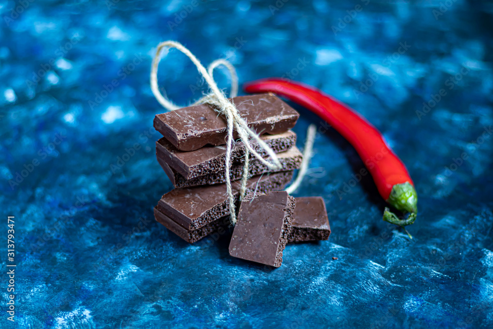 Dark porous chocolate with nuts on the table, closeup. Dark blue trend background 2020. In the background is red chili pepper. Dark porous chocolate with nuts on the table, closeup. Dark blue trend background 2020. In the background is red chili pepper.