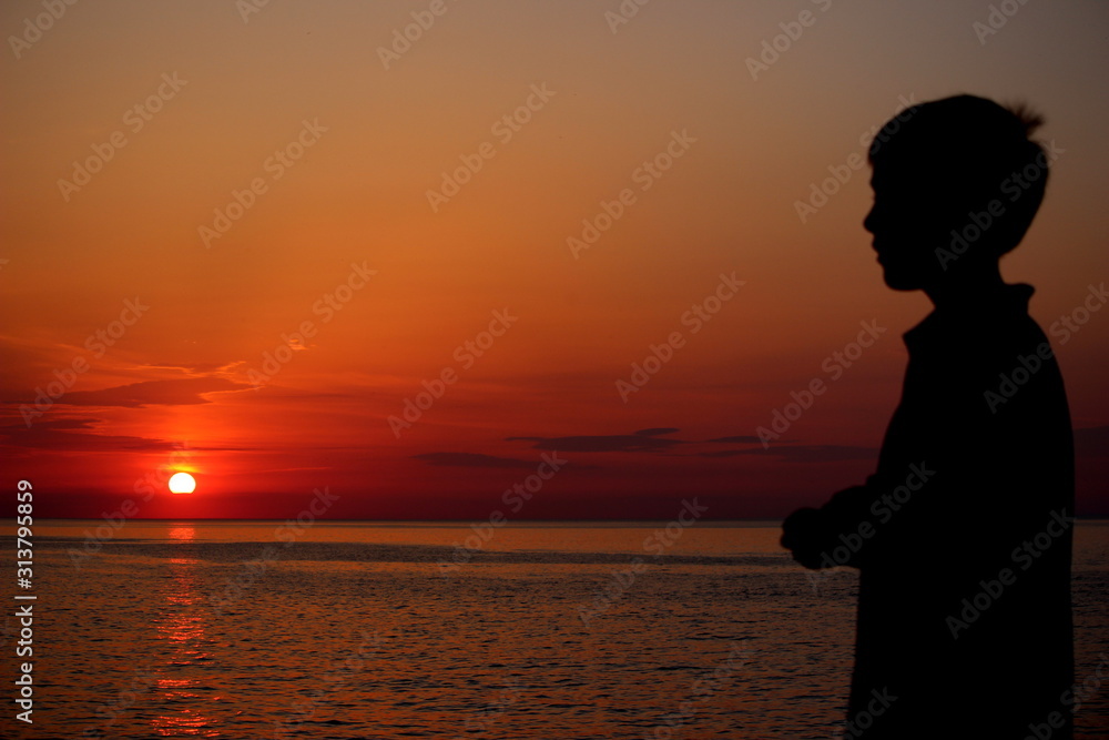Silhouette d'enfant admirant un coucher de soleil sur la mer